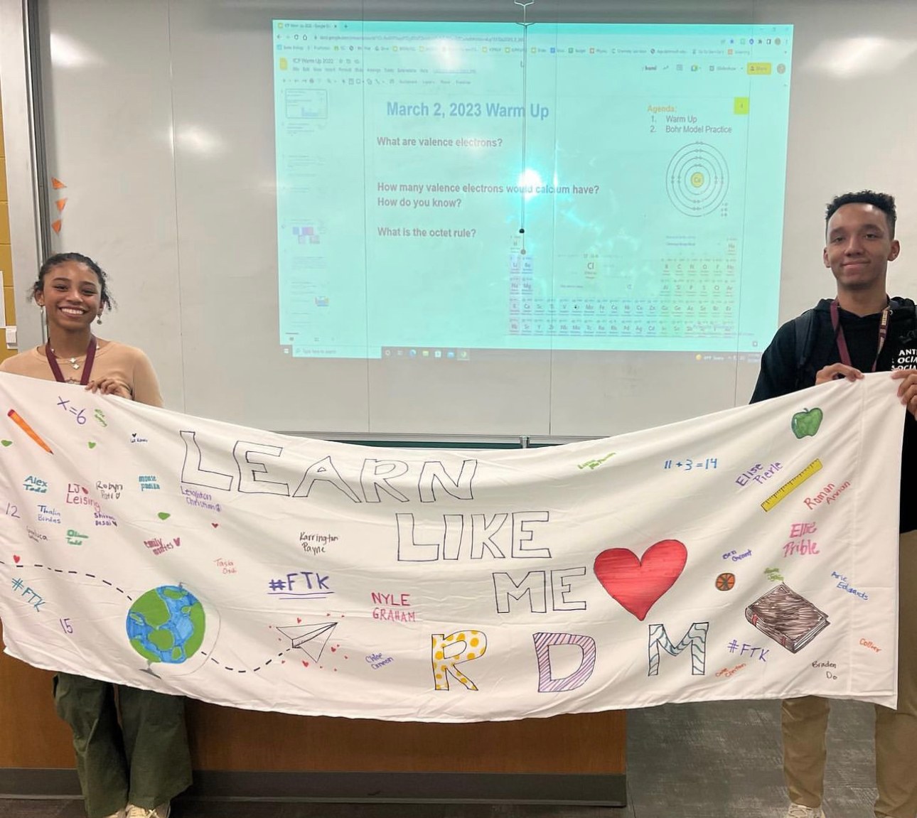 Students behind a hand-painted Learn Like Me banner