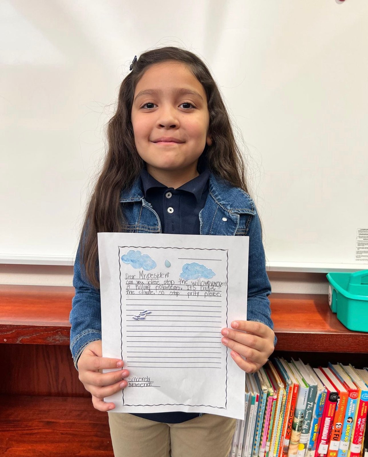 A student holding her work in front of the classroom wall